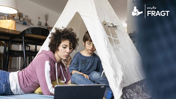 Eine Mutter und ein Kind sitzen in einem Spielzelt und schauen einen Film auf einem Tablet.