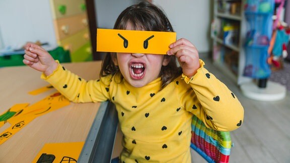 Ein Kind hält sich ein Papier vor die Augen und schreit