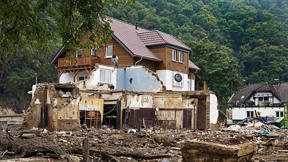 Ländliches Hotel im Ahrtal: Oberer Teil unversehrt, untere Etage verwüstet mit viel Schutt; im Hintergrund Wald