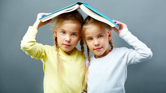Mädchen-Zwillinge unter einem Buch