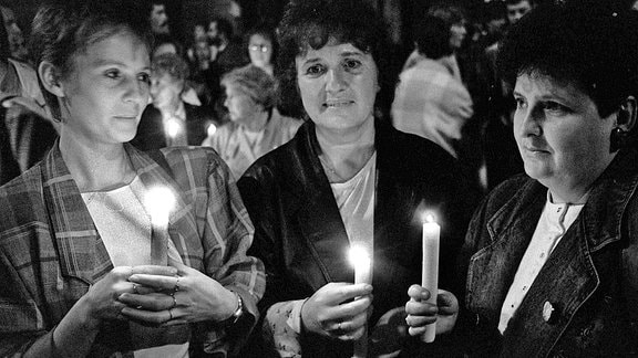Im Herbst 1989 stehen im Anschluss an ein Friedensgebet Teilnehmer mit Kerzen in der Hand vor der Nikolaikirche in Leipzig.